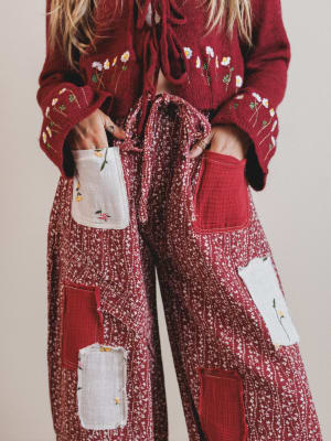 Person wearing a red sweater and patterned pants with patches on a neutral background