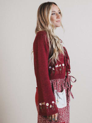 Woman wearing a burgundy cardigan with floral embroidery on a plain background