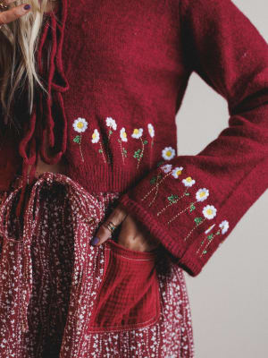 Red sweater with floral embroidery worn by a person against a neutral background