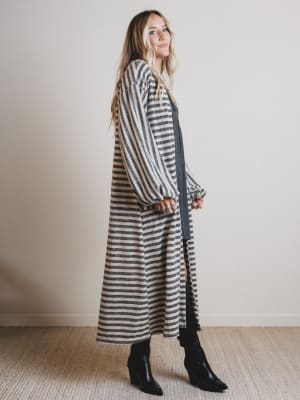 Woman wearing a long, dark gray and white striped dress with black boots against a plain background.