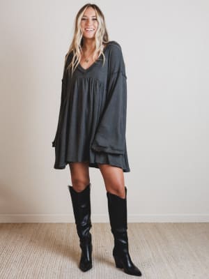 Woman wearing a dark gray dress and black knee-high boots indoors.