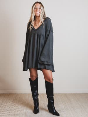 Woman wearing a dark gray dress and black knee-high boots indoors.