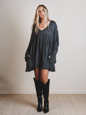 Woman wearing a dark gray dress and black knee-high boots against a plain background