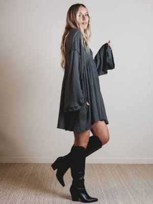 Woman wearing a dark gray dress and black knee-high boots against a plain background