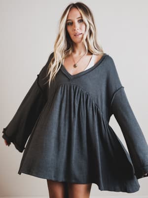 Woman wearing a dark gray dress with long sleeves against a plain background