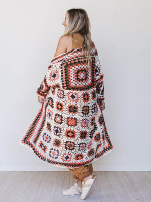 Person wearing a patterned crochet cardigan against a white wall