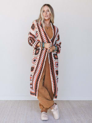 Woman wearing a patterned long cardigan over a brown outfit against a white background