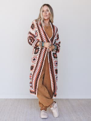 Woman wearing a patterned long cardigan over a brown outfit against a white background