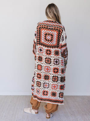 Person wearing a long, patterned crochet cardigan against a white background