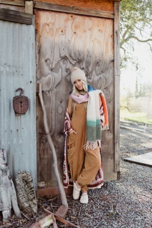 Person standing in front of a wooden shed with a scarf and hat