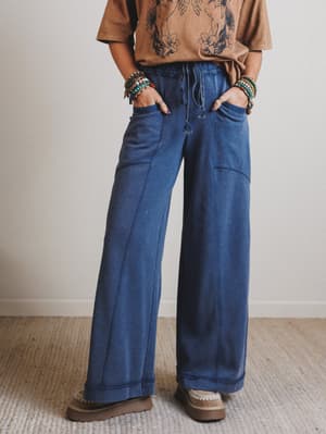 Person wearing blue wide-leg jeans and a brown shirt against a plain background