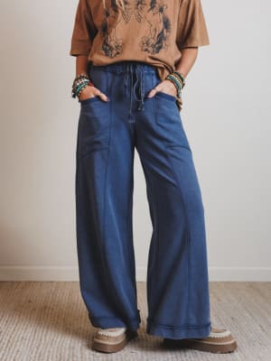 Person wearing a brown shirt and blue wide-leg pants with a neutral background