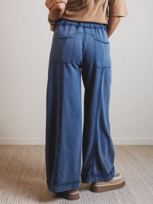 Person wearing blue wide-leg pants and a brown top on a neutral background