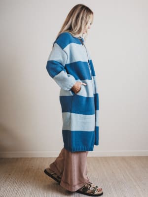 Person wearing a long blue and gray striped sweater against a plain background
