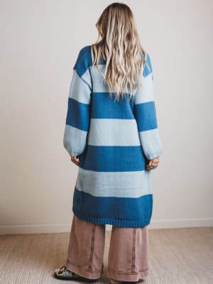 Person wearing a blue and gray striped sweater with brown pants against a plain background
