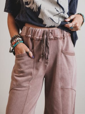 Person wearing a patterned top and brown pants with a neutral background