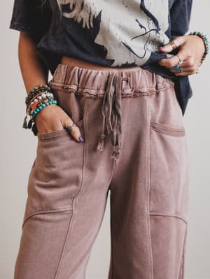 Person wearing a patterned top and brown pants with a neutral background