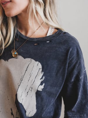 Person wearing a dark blue shirt with a graphic design, accessorized with a necklace.