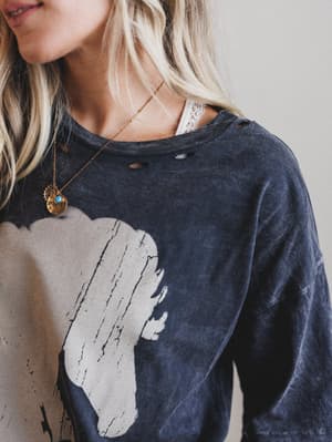 Person wearing a charcoal gray shirt with a graphic design, accessorized with a necklace.