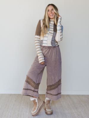 Woman wearing a patchwork striped sweater, brown wide-leg pants with crochet trim, and light brown platform boots.