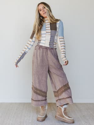 Woman wearing a patchwork striped sweater, brown wide-leg pants with crochet trim, and light brown platform boots.
