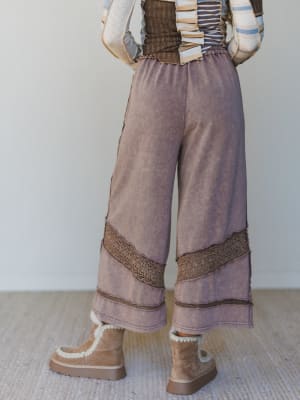 Person wearing wide-leg pants with decorative trim and brown boots on a neutral background
