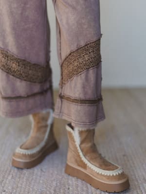 Brown platform boots with beige soles worn with patterned pants on a neutral background