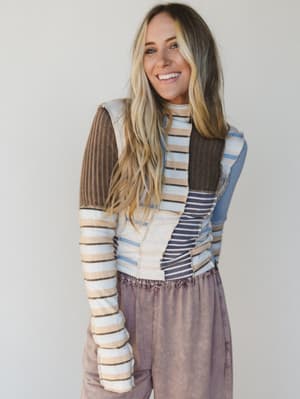 Woman wearing a colorful striped sweater and brown pants against a plain background
