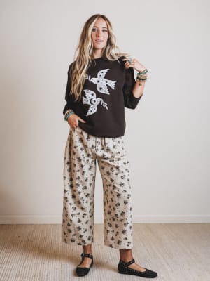 Woman wearing a black sweater with a white design and floral pants against a plain background
