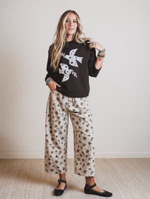 Woman wearing a black sweater with a white design and floral pants against a plain background