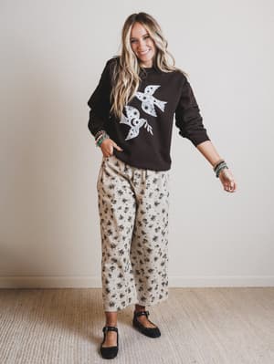 Woman wearing a black sweatshirt with a white design and patterned pants against a plain background