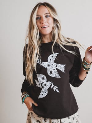 Woman wearing a black sweatshirt with white bird designs on a plain background