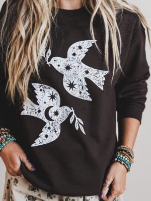 Black sweatshirt with white bird designs worn by a person with long hair and bracelets.