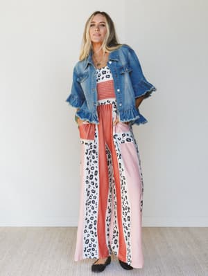 Woman wearing a denim jacket, patterned top, and wide-leg pants with a white background