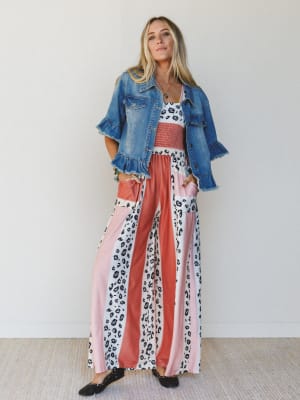 Woman wearing a denim jacket over a colorful, patterned, wide-leg jumpsuit against a white background