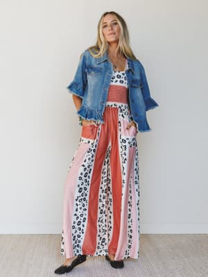 Woman wearing a denim jacket over a colorful, patterned, wide-leg jumpsuit against a white background