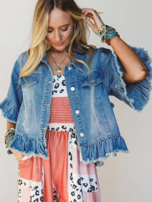 Woman wearing a denim jacket with ruffled sleeves against a plain background