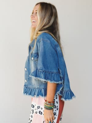 Woman wearing a denim jacket with ruffled details on a plain background