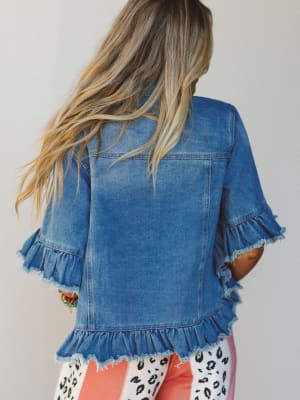 Person wearing a blue denim jacket with ruffled edges on a plain background
