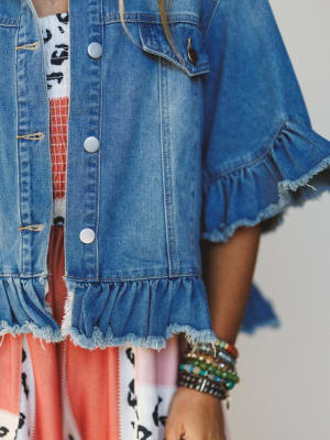 Close-up of a person wearing a blue denim jacket with ruffled edges on a plain background.