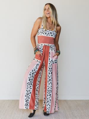 Woman wearing a colorful jumpsuit with leopard print and pink accents against a plain background
