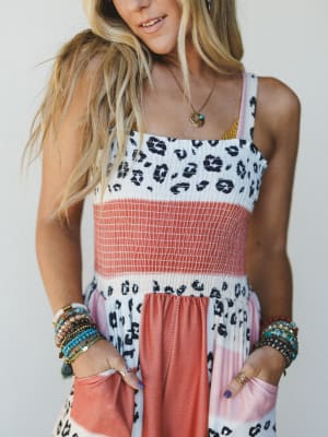 close-up of woman wearing a colorful jumpsuit with leopard print and pink accents against a plain background
