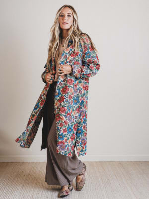 Woman wearing a long floral coat against a plain background