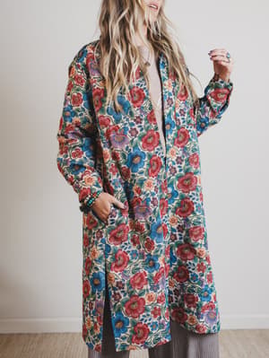 Person wearing a colorful floral coat against a plain background