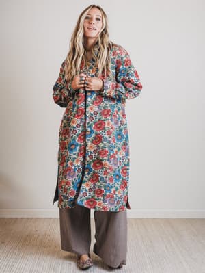 Woman wearing a colorful floral coat against a plain background