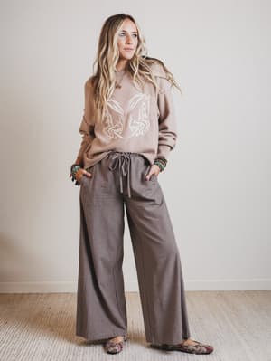 Woman wearing a brown sweater and wide-leg pants against a plain background