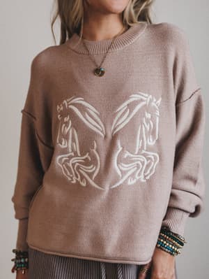 Person wearing a brown sweater with horse design against a neutral background