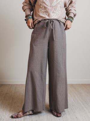 Person wearing a beige embroidered sweater and brown striped pants on a plain background