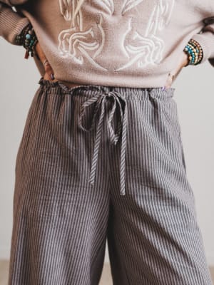 Person wearing a beige sweater with white abstract design and striped brown pants.