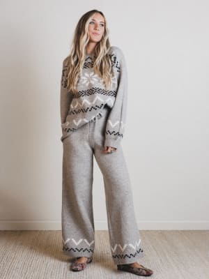 Woman wearing a patterned sweater and pants against a plain background
